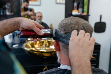An old man enjoing haircut by a master in a barbershop.  An old man gets a stylish haircut