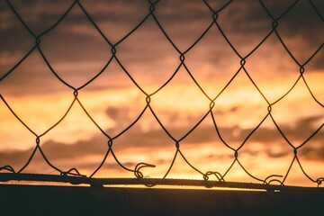 Wire mesh fence against cloudy sky at sunset