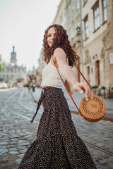 Happy smiling curly brunette woman wearing trendy summer outfit with round wicker shoulder rotan...