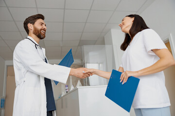 Obraz premium Two doctors in uniform shaking hands standing in clinic hall near reception