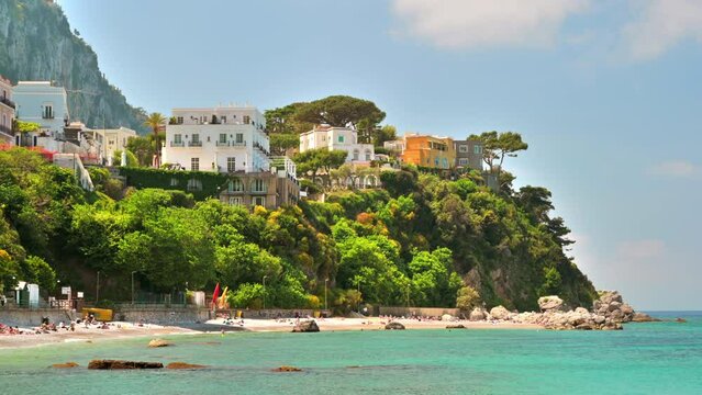 View of the Tyrrhenian sea coast in Capri, Italy. Classic buildings, beach with resting people, greenery