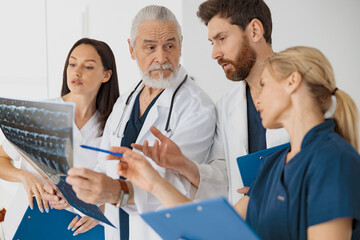 Group of doctors in uniform look and discuss an X-ray or MRI scan of patient spine