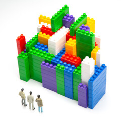 miniature people. figures of people stand near the colored blocks of a plastic constructor on a white background in the form of multi-storey buildings. concept of modern buildings and houses