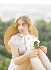 Close up portrait of a sweet blonde with a white peony in her hands at sunset.