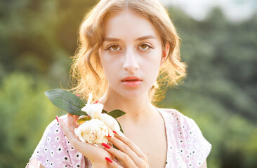 Close up portrait of a sweet blonde with a white peony in her hands at sunset.