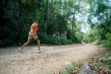 Naklejka na ściany i meble Man in orange t-shirt running on a countryside road. Side view.