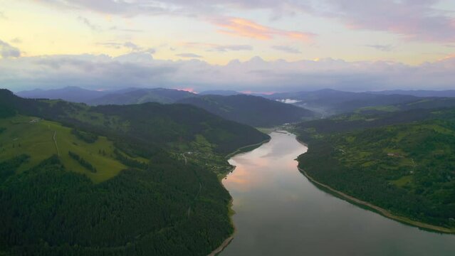 Aerial drone view of nature in the Carpathians in Romania at sunset. Lake Izvorul Muntelui located in a valley, hills covered with lush forest
