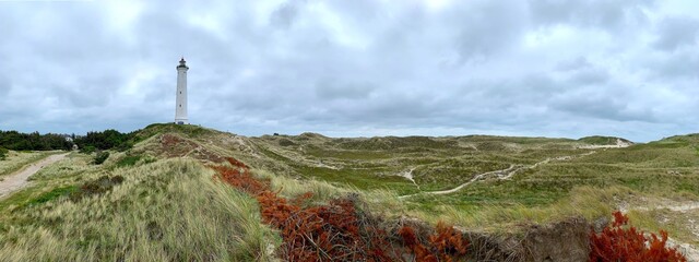white lighthouse Lyngvig Fyr in a beautiful dune landscape with a sandy trail at a cloudy day,...