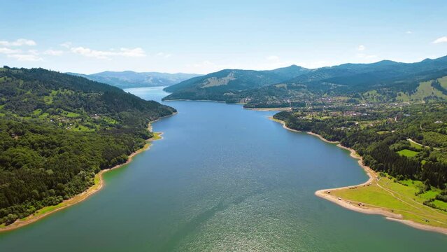Aerial drone view of nature in the Carpathians in Romania. Lake Izvorul Muntelui and a village located in a valley, hills covered with lush forest
