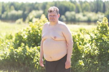 A fat man with a big belly near the house is trying to do physical exercises.