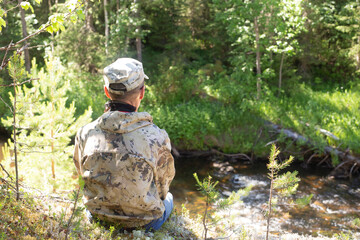 A man is sitting on the bank of a forest river.Contemplation of the forest and the river, outdoor recreation.