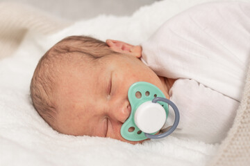 Sleeping newborn baby with pacifier white blanket, an emotional portrait of 7 days old baby