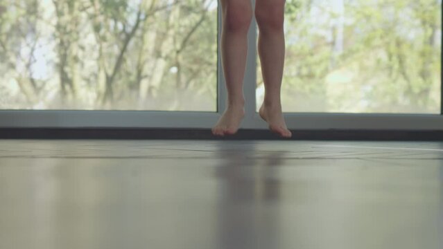 barefoot legs jumping child on floor indoors, valgus heels flat-feet foot problem. happy kid jumping with big windows behind. x-knees or knock knees on children toddler, orthopedic ortho kid health 