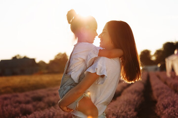 family day. young mom and little daughter enjoy relaxing in a field with lavender at sunset. A...