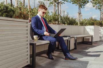 Young man in eyeglasses working on laptop outdoors.