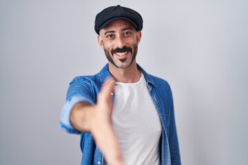 Hispanic man with beard standing over isolated background smiling friendly offering handshake as greeting and welcoming. successful business.