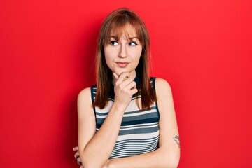 Redhead young woman wearing casual t shirt with hand on chin thinking about question, pensive expression. smiling with thoughtful face. doubt concept.