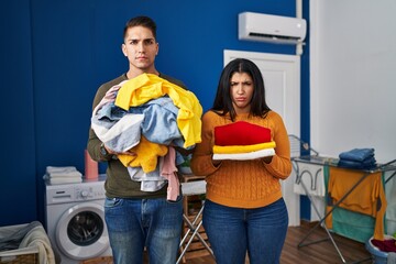 Young couple holding laundry dirty and clean laundry skeptic and nervous, frowning upset because of problem. negative person.