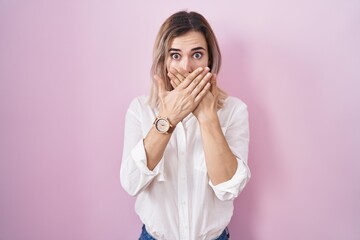 Young beautiful woman standing over pink background shocked covering mouth with hands for mistake. secret concept.