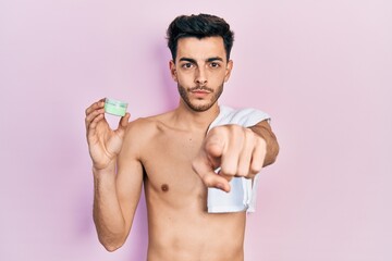 Fototapeta premium Young hispanic man shirtless wearing towel and eye bags patches pointing with finger to the camera and to you, confident gesture looking serious