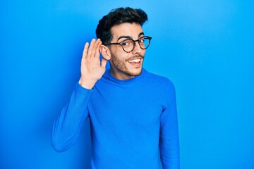 Young hispanic man wearing casual clothes and glasses smiling with hand over ear listening an...