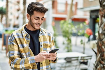 Handsome hispanic man smiling happy and confident at the city using smartphone