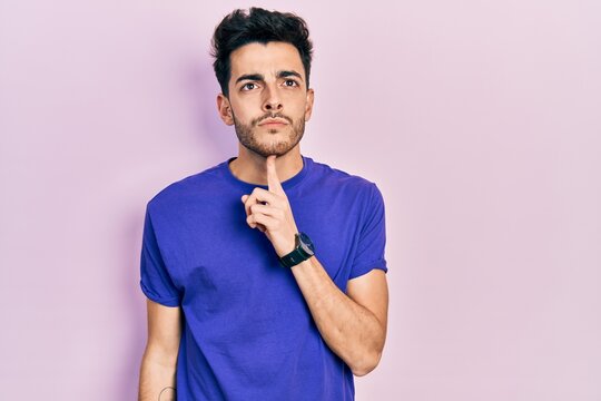 Young hispanic man wearing casual t shirt thinking concentrated about doubt with finger on chin and looking up wondering