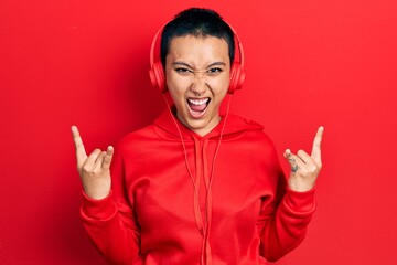 Naklejka premium Beautiful hispanic woman with short hair listening to music using headphones shouting with crazy expression doing rock symbol with hands up. music star. heavy concept.