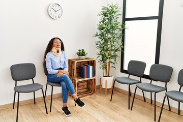 Young latin woman wearing neck collar sitting on chair at clinic waiting room