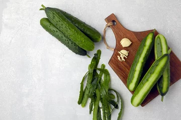 Fotobehang Fresh cucumbers with skin and knife on a brown wooden cutting board on a light gray concrete table © OneBit