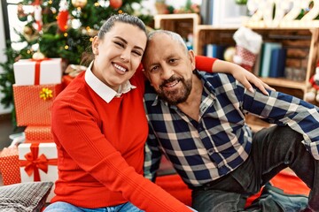 Young daughter and senior father together celebrating christmas at home, sitting by christmas tree around festive ornaments