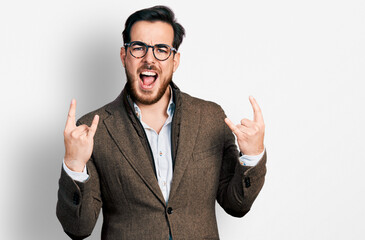 Young hispanic man wearing business jacket and glasses shouting with crazy expression doing rock symbol with hands up. music star. heavy concept.