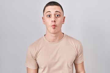 Young man standing over isolated background making fish face with lips, crazy and comical gesture. funny expression.