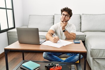 Obraz premium Hispanic man doing papers at home thinking concentrated about doubt with finger on chin and looking up wondering
