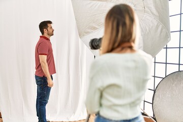 Obraz premium Woman photographer talking pictures of man posing as model at photography studio looking to side, relax profile pose with natural face with confident smile.