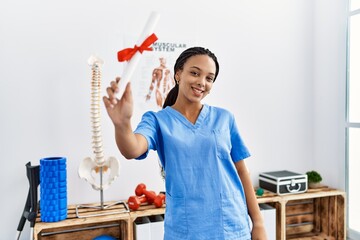 Young african american woman wearing physio therapist uniform holding diploma at clinic