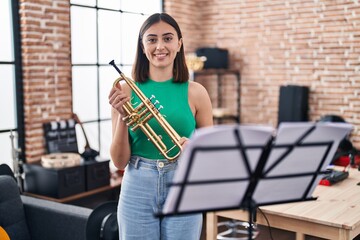 Young hispanic woman musician holding trumpet at music studio