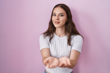 Young hispanic girl standing over pink background smiling with hands palms together receiving or giving gesture. hold and protection