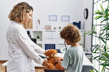 Mother and son wearing doctor uniform auscultating teddy bear at clinic
