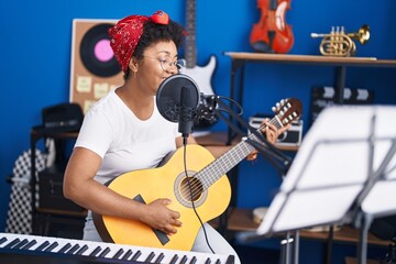 Fototapeta na wymiar African american woman musician singing song playing classical guitar at music studio