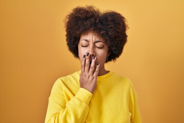 Fototapeta na wymiar Young african american woman standing over yellow background bored yawning tired covering mouth with hand. restless and sleepiness.