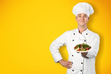 Young man standing and holding plate or dish on yellow background