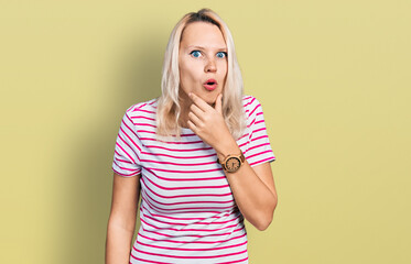 Young caucasian woman wearing casual clothes looking fascinated with disbelief, surprise and amazed expression with hands on chin