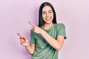 Beautiful woman with blue eyes wearing casual t shirt smiling and looking at the camera pointing with two hands and fingers to the side.