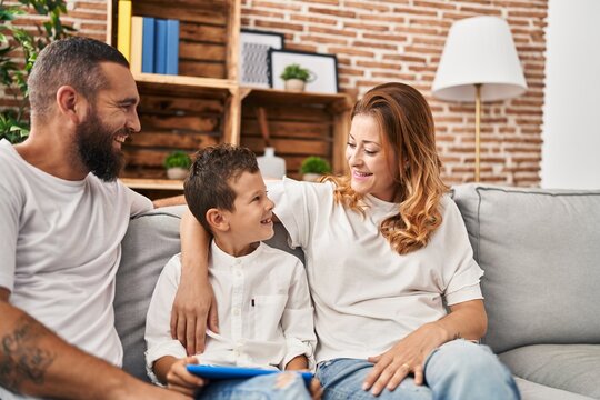 Family using touchpad hugging each other sitting on sofa at home