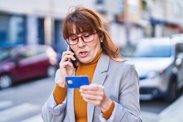 Middle age woman business executive talking on the smartphone holding credit card at street