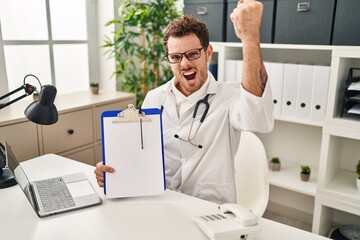 Fototapeta na wymiar Young hispanic man wearing doctor stethoscope holding clipboard annoyed and frustrated shouting with anger, yelling crazy with anger and hand raised