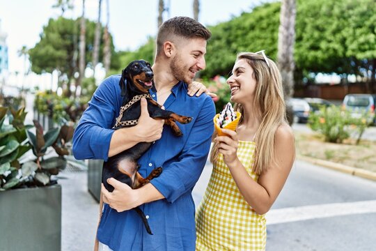 Young caucasian couple eating ice cream smiling happy with dog at the city.