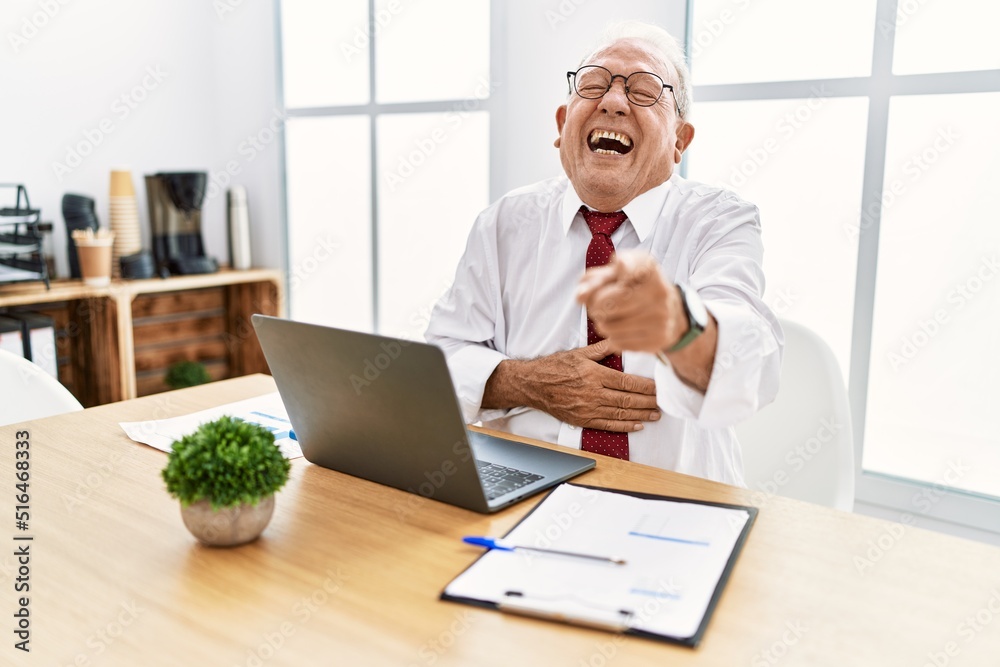 Sticker Senior man working at the office using computer laptop laughing at you, pointing finger to the camera with hand over body, shame expression