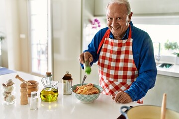 Senior man smiling confident pouring oregano on spaghetti at kitchen